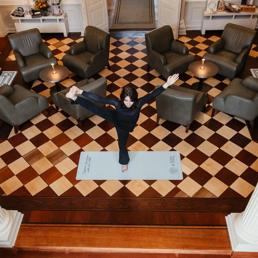 A yoga session on a single mat in a hotel lounge with a chequerboard floor